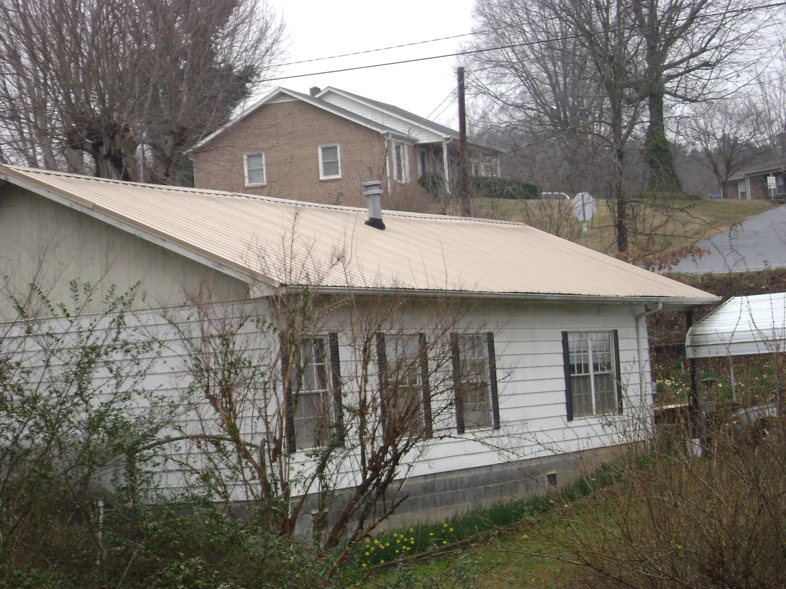 Tan metal roof on a white sided house set into a hillside — Commercial Roofing by Roofing Brothers in Seabrook